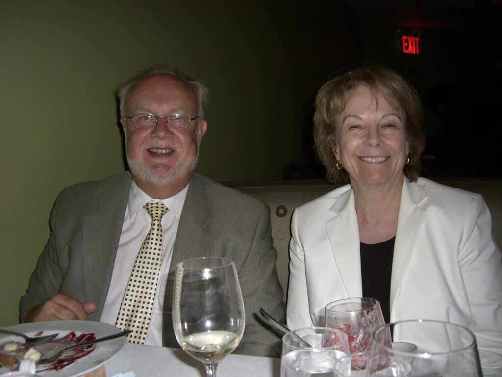 Jan Peter Strömgren och Brenda Battat sitter vid ett middagsbord och ler in i kameran. De är finklädda i kavaj och Jan-Peter har slips. Bakom dem syns en röd Exit-skylt.