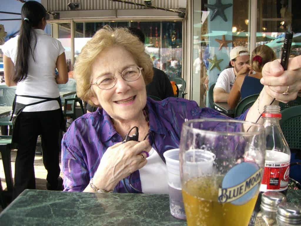 Marcia Dugan, IFHOH sitter utomhus vid ett cafébord med en mugg coca-cola framför sig. Hon håller fram en mick med ena handen och håller i en mottagare med den andra. På bordet står även en flaska coca-cola och ett glas öl. I bakgrunden syns flera cafégäster och en servitris.