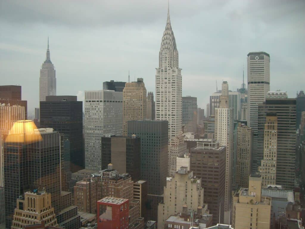 Bild över gråmulet New York i aug 2006, tagen från ett hotellrum. En lampa speglar sig i fönstret. Bland annat syns Empire state building och Chrysler building.